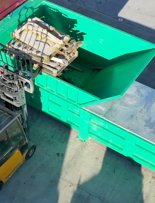 Forklift feeding wooden pallets into the Gradeall G140 Pre-Crush Compactor's open top hopper