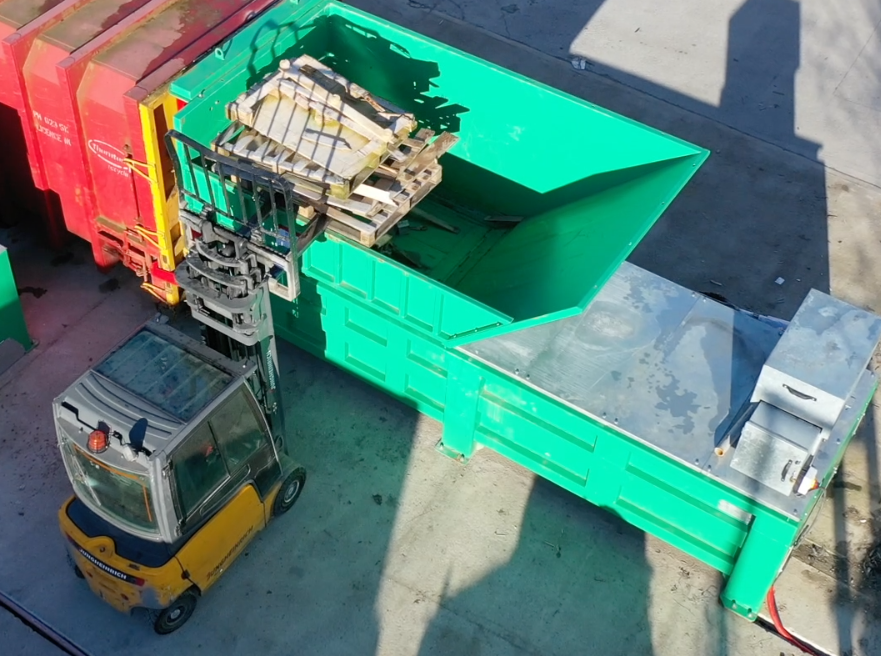 Forklift feeding wooden pallets into the Gradeall G140 Pre-Crush Compactor's open top hopper