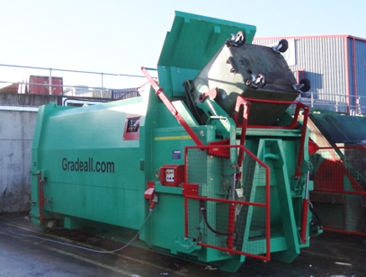 Gradeall GPC P24 portable wet waste compactor in operation, lifting and emptying a bin outside a supermarket warehouse