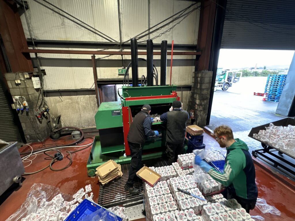 Workers operating a Gradeall Can Baler amidst an array of aluminium cans ready for recycling.