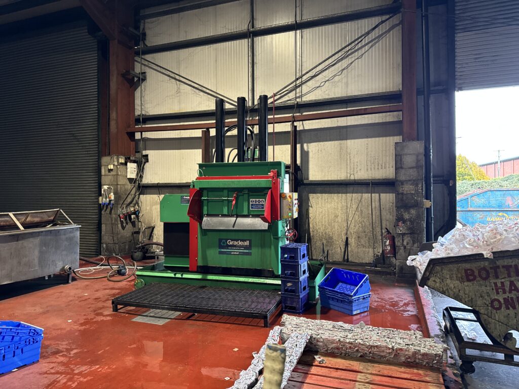 The Gradeall Can Baler situated in an industrial recycling facility, with baled aluminium cans in the foreground.