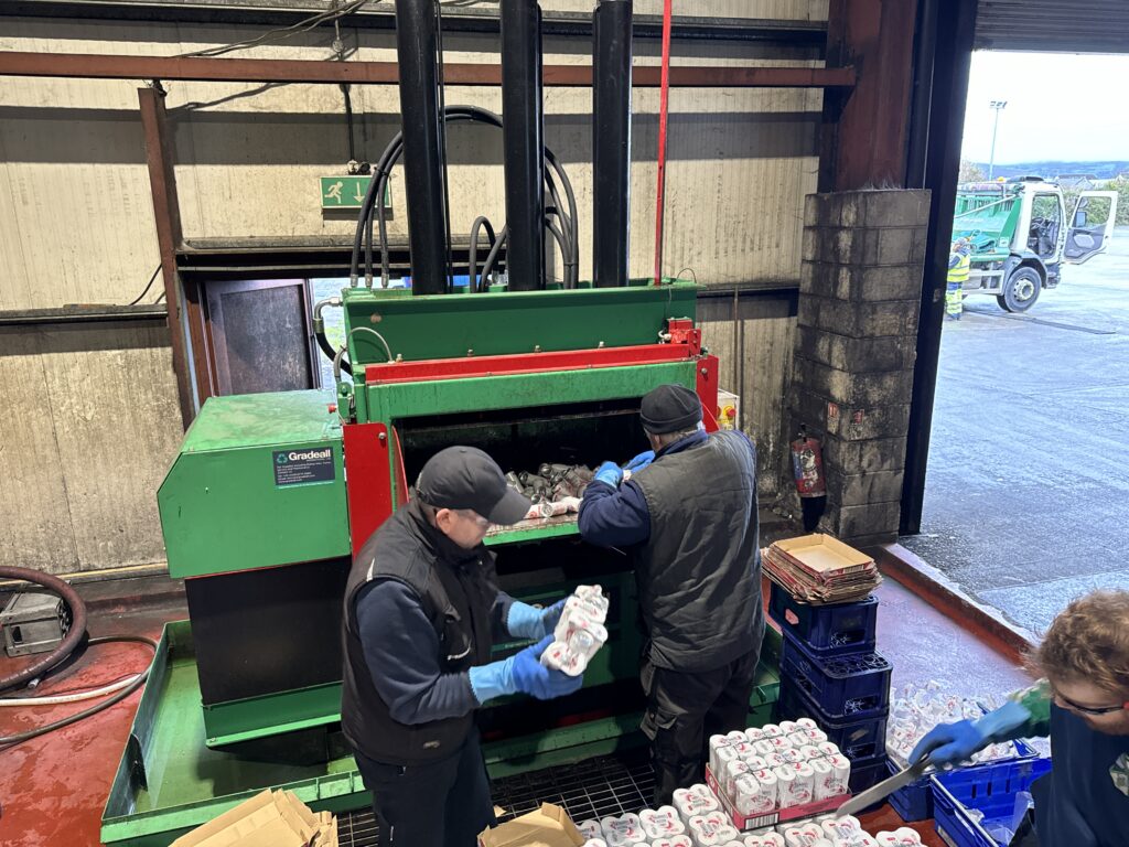 Workers sorting and loading drinks cans into the Gradeall Can Baler for recycling.