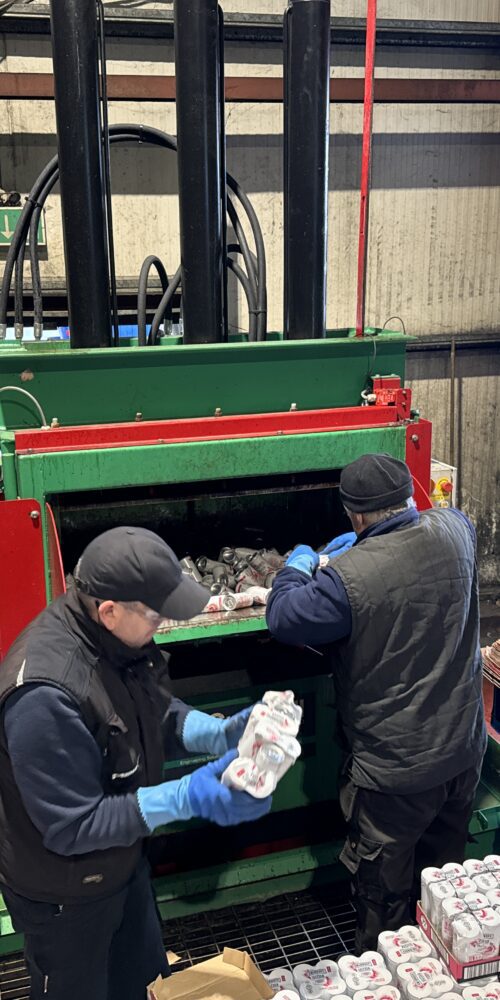 Workers sorting and loading drinks cans into the Gradeall Can Baler for recycling.