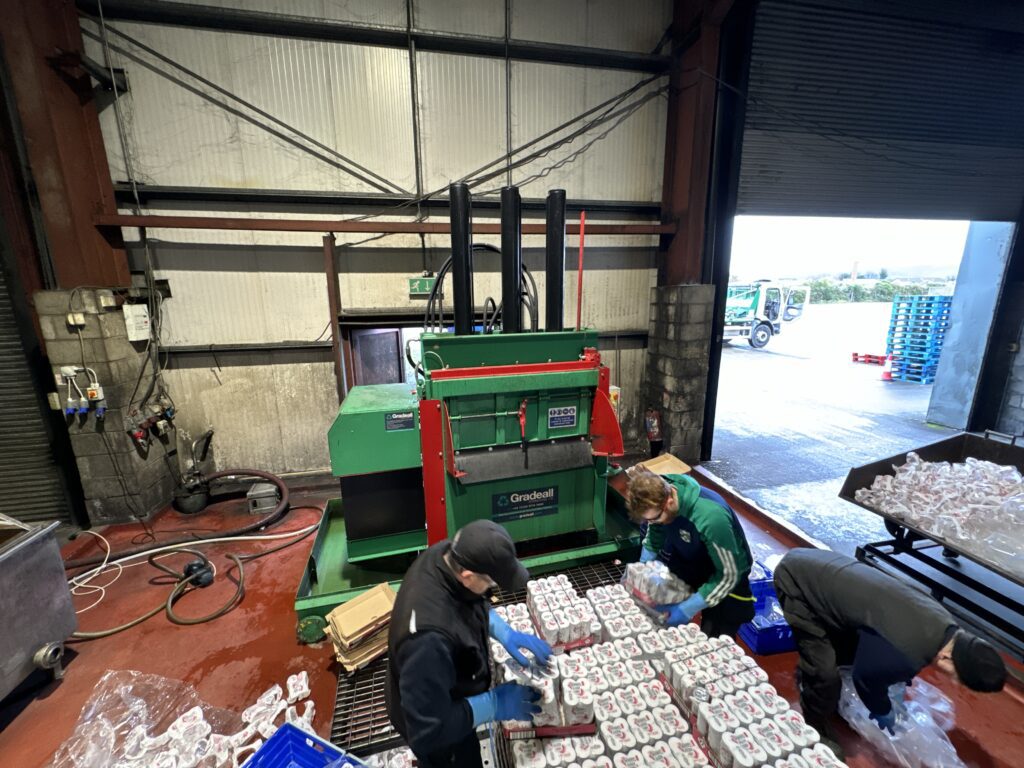 Workers feeding a baler machine with cans for recycling at a recycling facility using gradeall can baler.