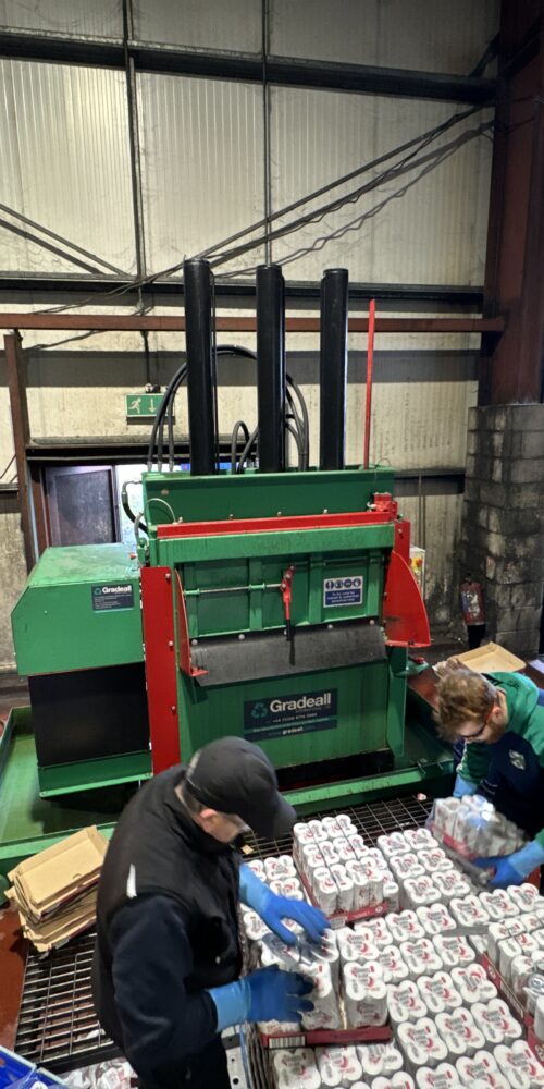 Workers feeding a baler machine with cans for recycling at a recycling facility using gradeall can baler.