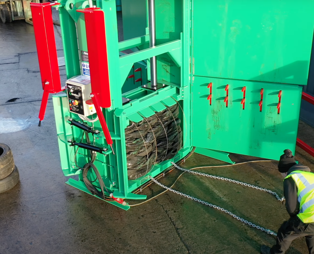 Worker installing baling wires on a tyre bale in a Gradeall MK2 tyre baler to secure the load.