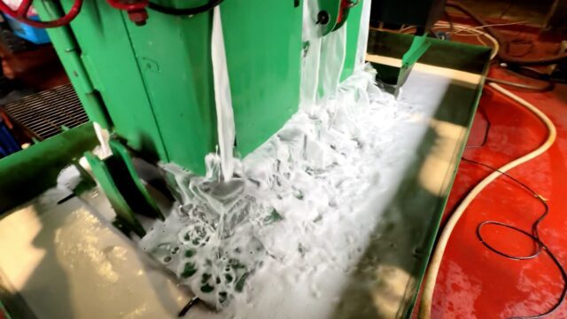 Foamy liquid drains from a can baler's sump as it processes beverage cans.