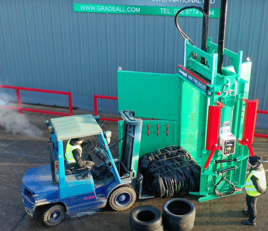 Forklift lifting a completed tyre bale from a Gradeall MK2 tyre baler for removal.