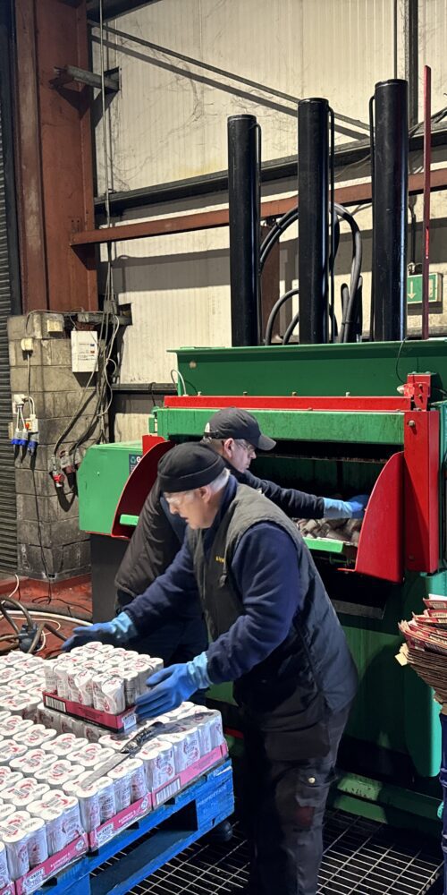Workers at a recycling facility loading drinks cans into a Gradeall Can Baler.