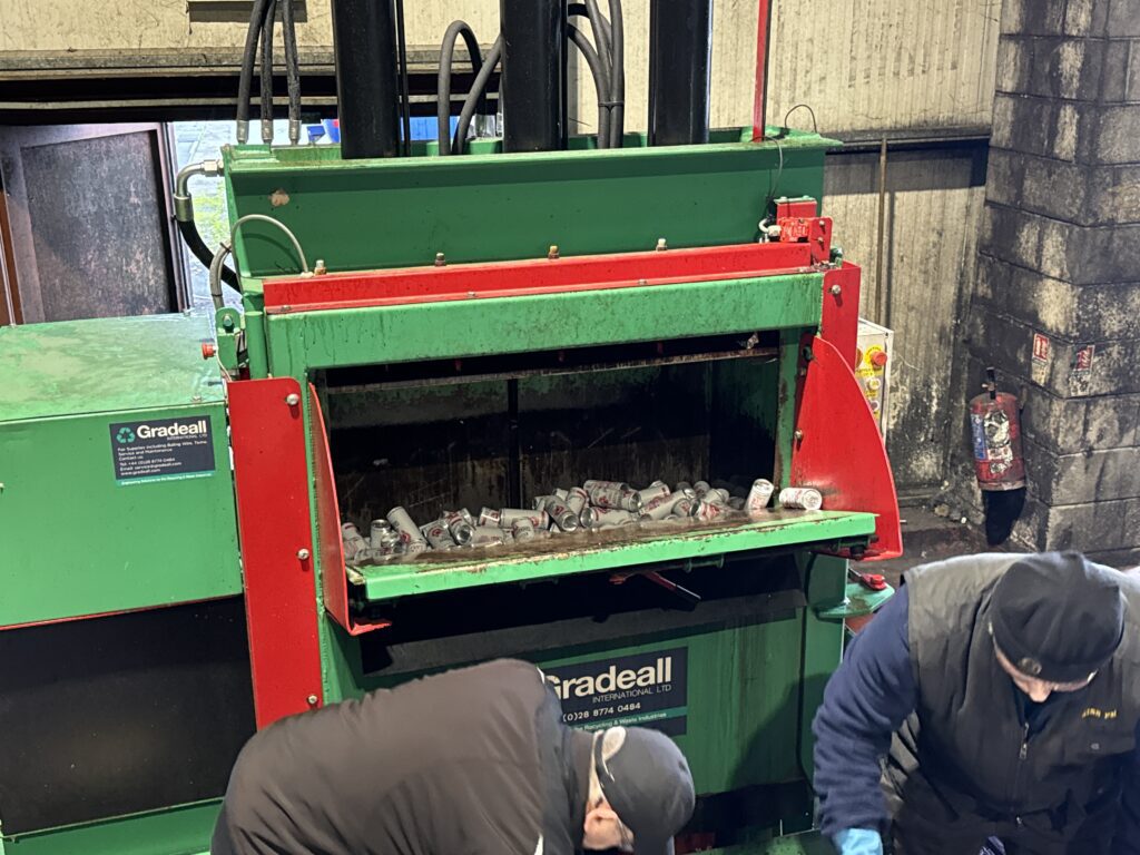 Workers loading a drinks can into the Gradeall can baler for crushing and recycling.