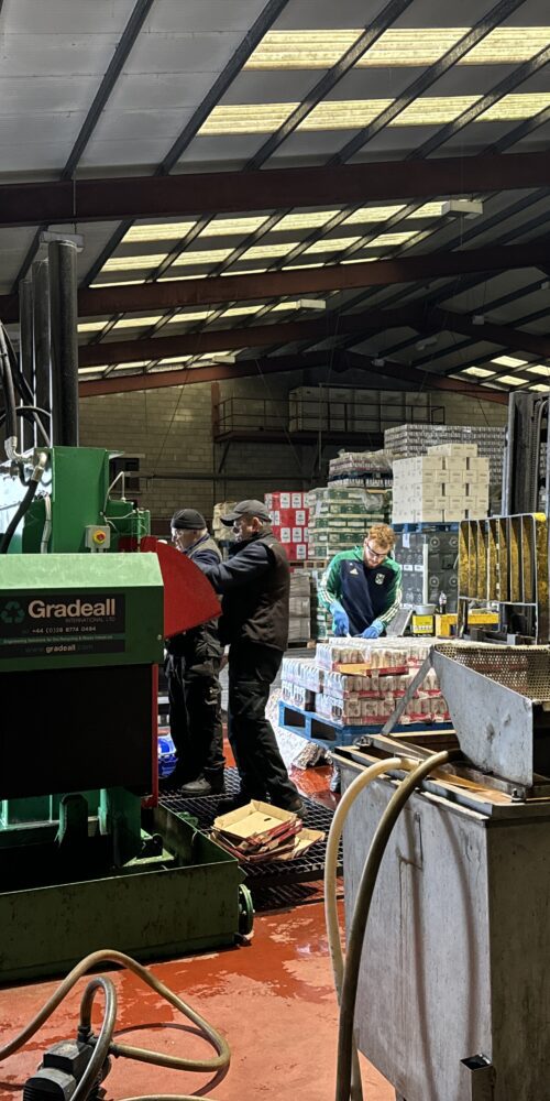 Workers at a facility loading drinks cans into a Gradeall can baler for recycling.