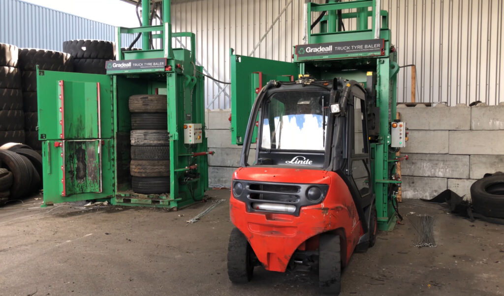 A forklift in front of two Gradeall Truck Tire Balers at a recycling facility.