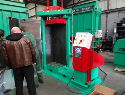 Industry professionals gather around a Gradeall clothes baler, showcasing the machine's large capacity