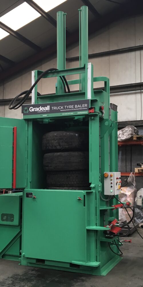 Workers operating a Gradeall Truck Tyre Baler in a manufacturing setting.