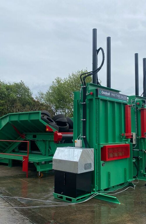 Two MK2 tyre balers positioned in front of a Gradeall inclined tyre baler conveyor in an outdoor industrial environment.