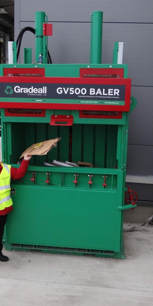 Worker loading cardboard into the Gradeall GV-500 baler machine.