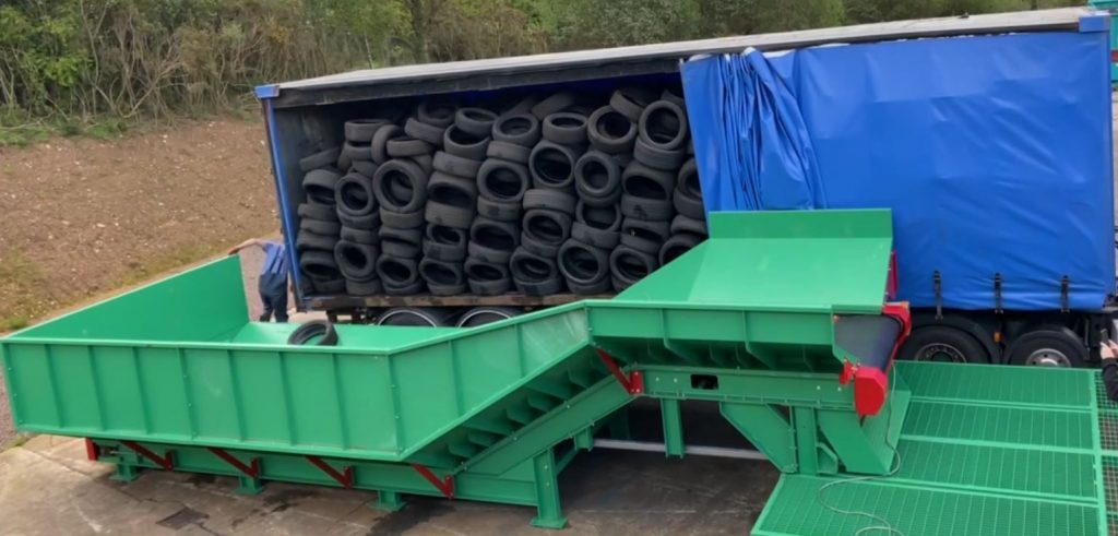Loose tyres being efficiently offloaded from a curtain side trailer onto a Gradeall inclined tyre baler conveyor, showcasing the direct unloading feature that streamlines the recycling process