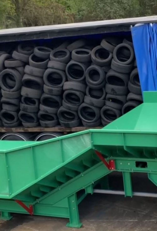 Loose tyres being efficiently offloaded from a curtain side trailer onto a Gradeall inclined tyre baler conveyor, showcasing the direct unloading feature that streamlines the recycling process