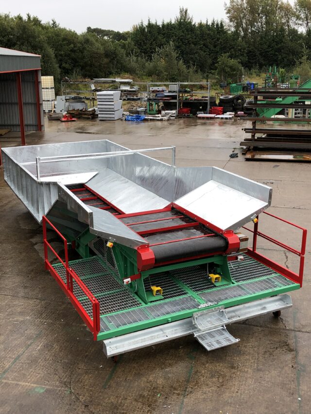 Photo of a Gradeall inclined tyre baler conveyor on a wet industrial yard, with a metal hopper and safety railings.