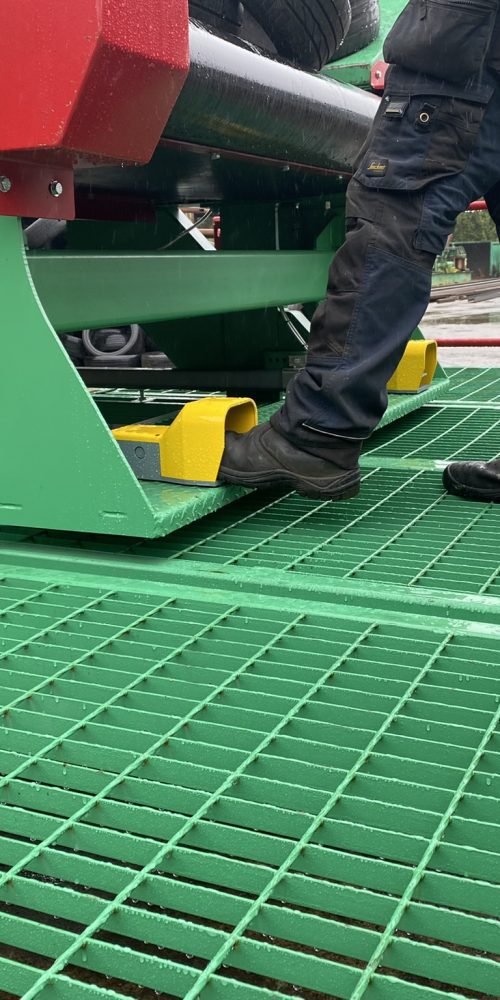 Close-up of an operator's feet on the safety grating of a Gradeall inclined tyre baler conveyor, utilizing foot-operated controls for tyre movement.