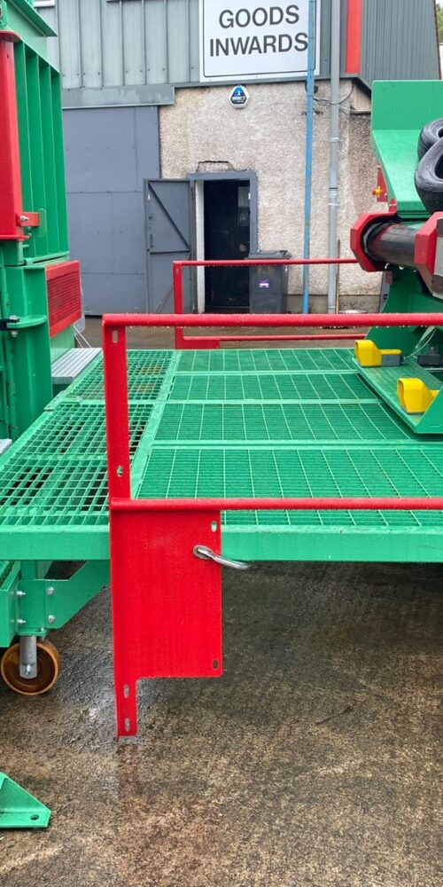 Close-up of the Gradeall inclined tyre baler conveyor's sliding platform with safety grating and a green and red machine part.