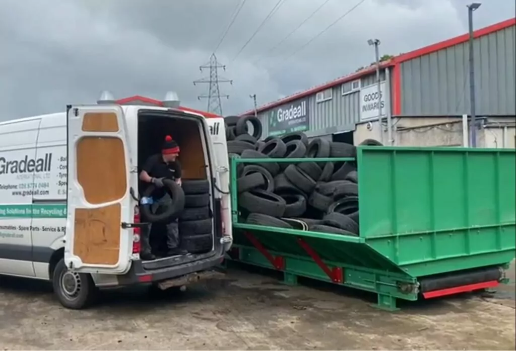 A Gradeall van parked beside an inclined tyre baler conveyor, loaded with waste tyres, illustrating the ease of loading tyres directly onto the conveyor.